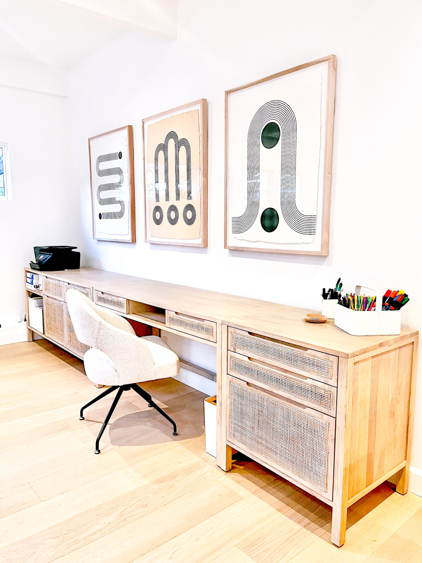 A wooden desk with two chairs and three framed pictures on the wall.