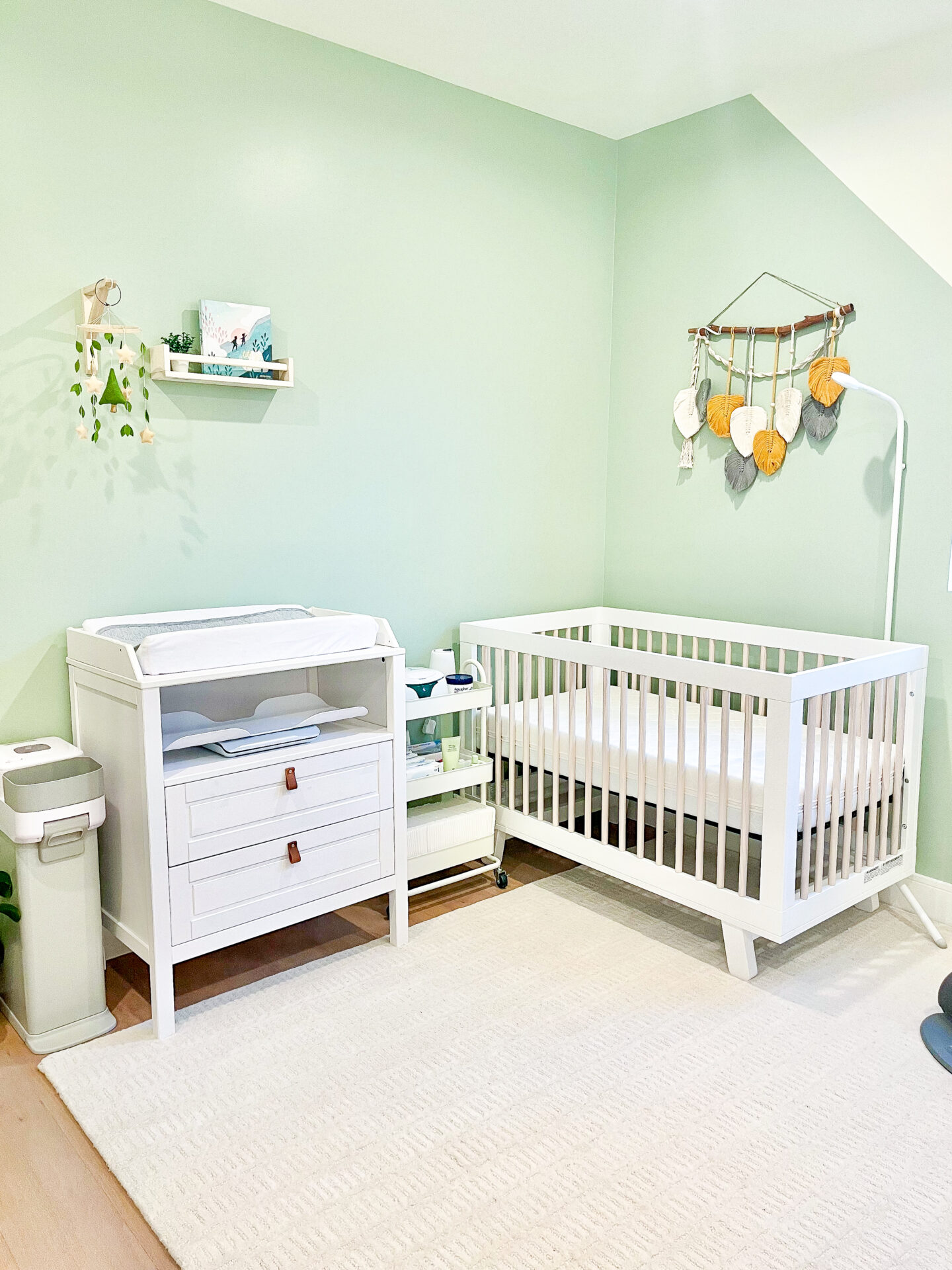 A baby room with green walls and white furniture.